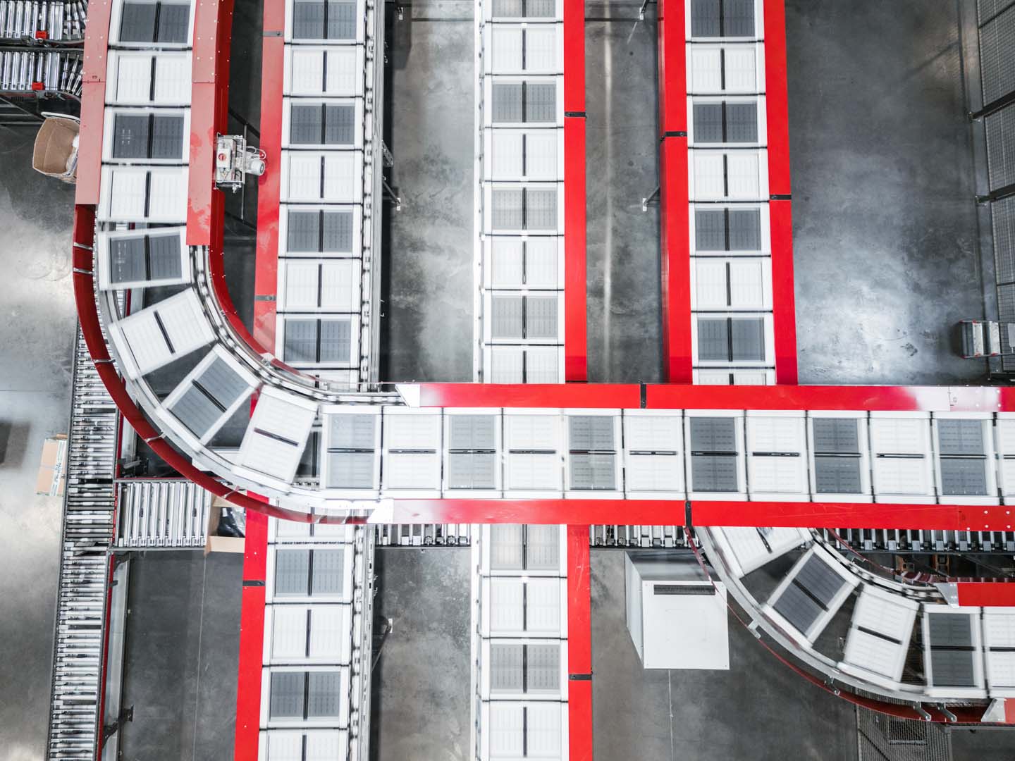 Top view of a conveyor belt system with red and white sections winding through an industrial warehouse, creating curved and straight paths across a gray concrete floor