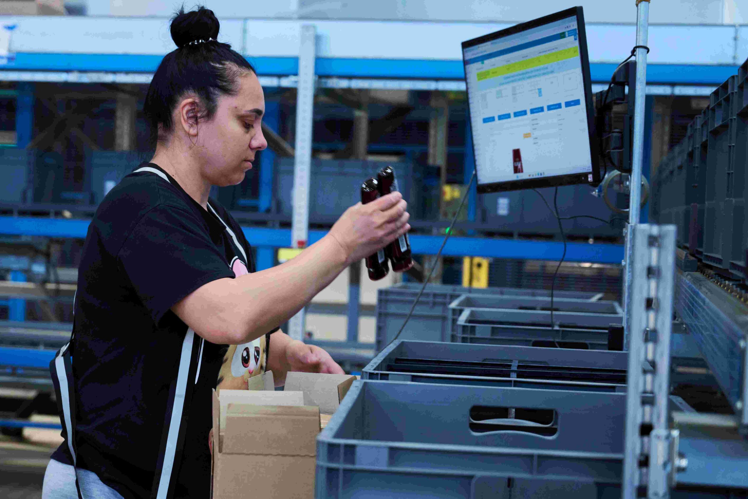 Eine Frau packt Haarshampoo von einem Wareneingangskarton in einen Lagerbehälter bei eMAG im Lager.