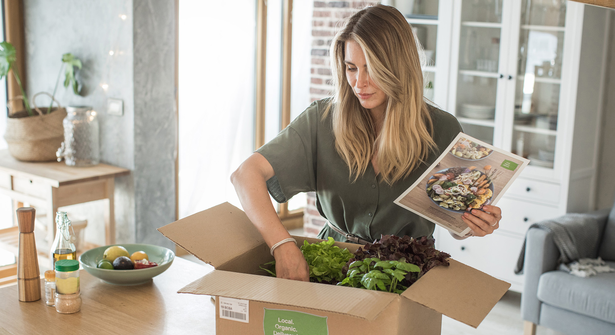 Eine Frau öffnet ein Karton mit frischen Lebensmitteln.