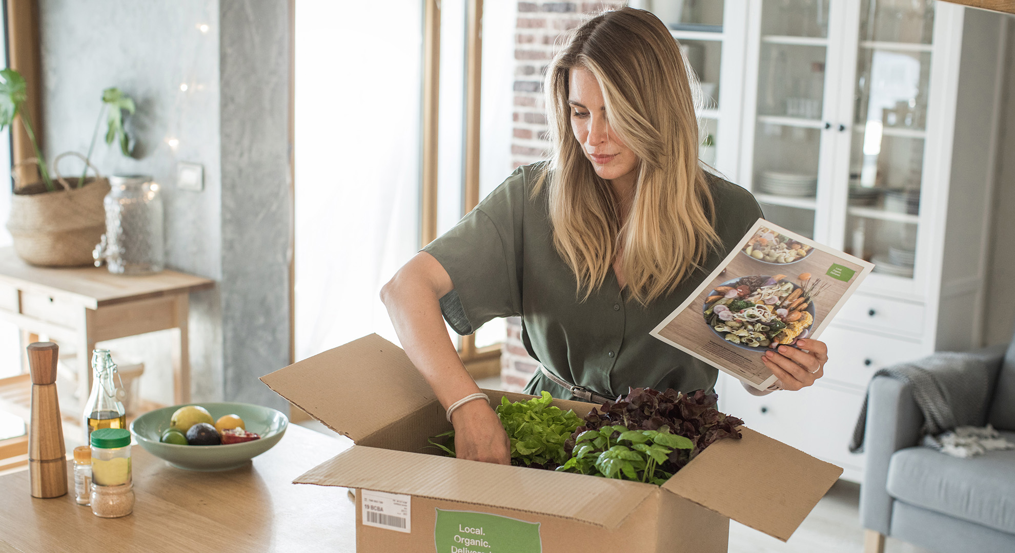 A woman is opening a carton containing fresh groceries.