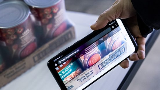 Das Bild zeigt eine Person, die ein Tablet bedient. Am Screen ist die KiSoft Genomix App zu sehen. Im Hintergrund Karton mit Artikeln. Der Mitarbeiter erfasst mithilfe der App alle relevanten Attribute des Artikels, der im Hintergrund abgebildet ist.