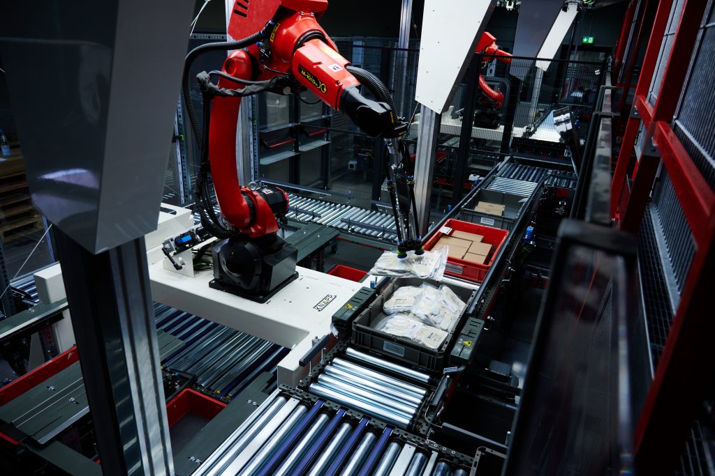 Un robot totalmente automatizado sujeta un artículo y lo coloca en una caja de destino. El Pick-it-Easy-Robot asume la preparación de artículos a toda hora y respalda al personal en el almacén.