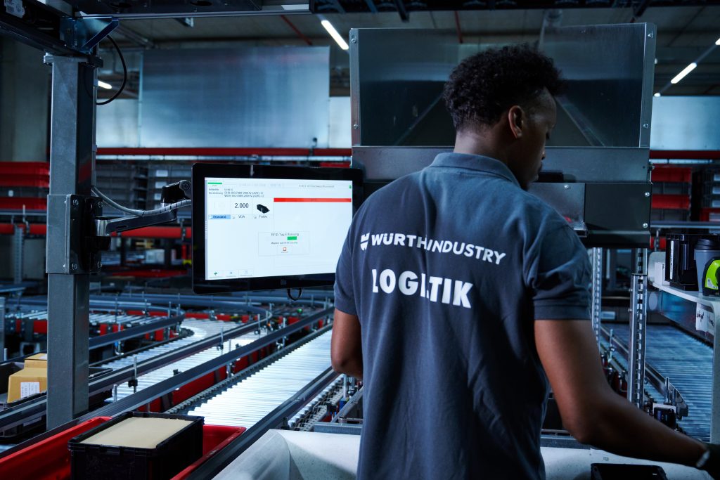 Puesto de trabajo Pick-it-Easy en Würth Industrie Service (WIS) Un empleado está frente al puesto de trabajo Pick-it-Easy y prepara los pedidos según el principio "mercancía a la persona".
