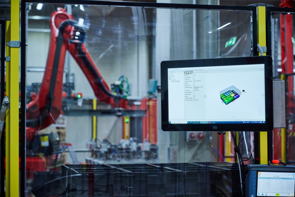 Auf einem Bildschirm wird das Packbild angezeigt, welches der Roboter im Hintergrund auf der Palette zusammenstellt. Die Softwarelösungen von KiSoft übernehmen eine zentrale Funktion in der Automatisierungslösung.