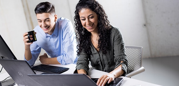 Two young adults are sitting at a desk and typing on their laptops.