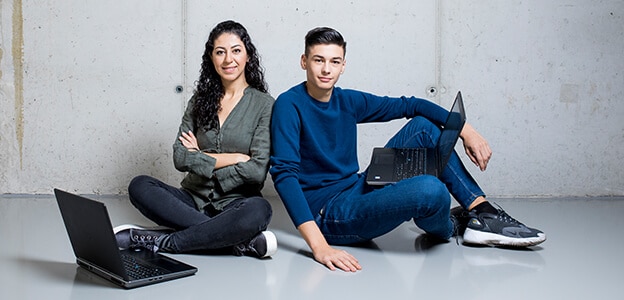 Zwei junge Menschen sitzen am Boden mit dem Laptop.