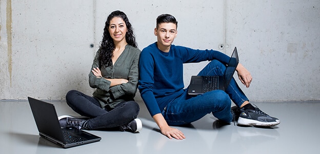 Deux jeunes gens sont assis par terre près de leurs ordinateurs.