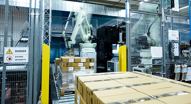 A palletizing robot in the Parfums Christian Dior warehouse places cartons on pallets in the dispatch area. The software for calculating the packing arrangement determines the right packing pattern. The fully automatic robot palletizing enables stable pallets.