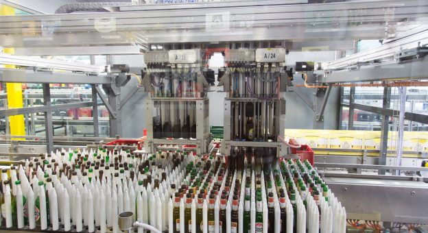 A large number of unsorted single bottles can be seen in the foreground. In the center of the image is a robot with grippers taking single bottles out of beverage crates for sorting.