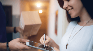 A woman receives the goods she has ordered online. The package has been delivered to her home and she is signing for it.