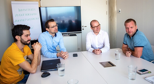 Vier Personen sitzen am Tisch und sprechen miteinander.