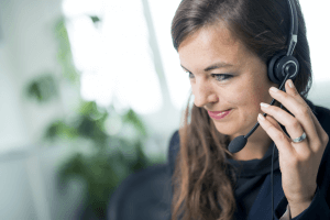 Femme du Service Desk SAP® EWM 24h/24 7j/7 qui porte un micro-casque et qui assiste les clients avec leurs questions et leurs problèmes après une mise en place de SAP® EWM. 