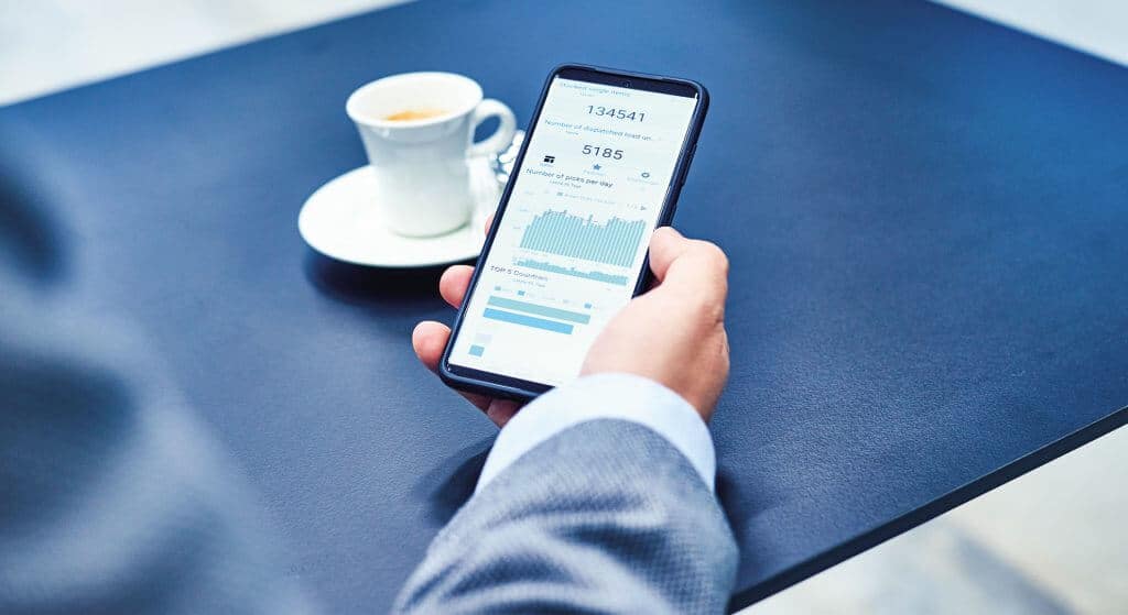 Logistikbetreiber hält Smartphone zur Analyse von Logistik KPIs mit der Software KiSoft Analytics. Zu sehen sind unterschiedliche Dashboards und Daten. Mit KiSoft Analytics behält der den Überblick über die Prozesse und kann die richtigen Entscheidungen für Lager und Supply Chain treffen.