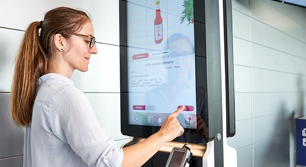 A woman stands at an order terminal and selects products with her hand - innovative technology