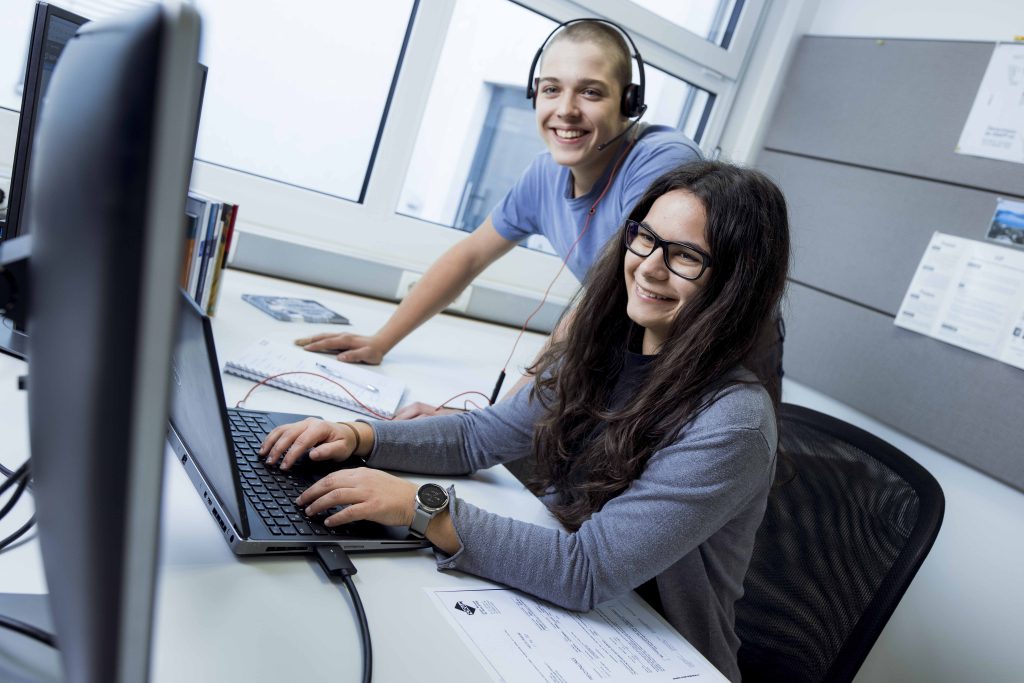 Zwei Lehrlinge schauen gemeinsam auf den Computer und lachen