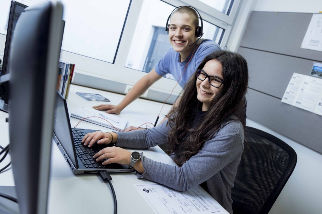 Lehrberuf Industriekauffrau:mann Zwei Lehrlinge schauen gemeinsam auf den Computer und lachen