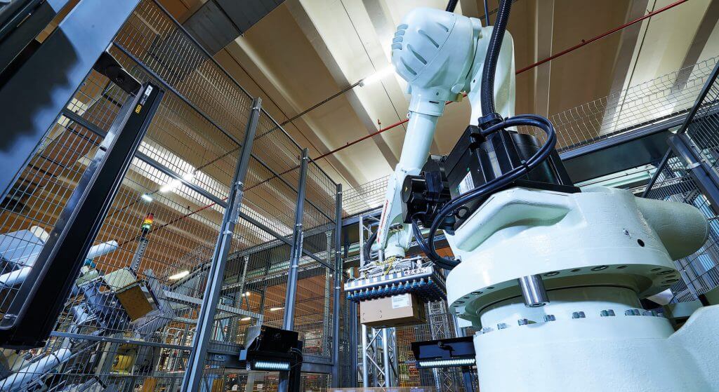 Un robot para el paletizado y despaletizado automáticos deposita una caja de cartón sobre un palet. Este paletizado totalmente automatizado libera de trabajo a los empleados.