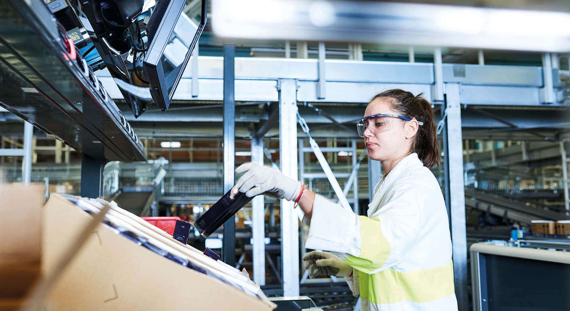 Employee at Parfums Christian Dior uses the ergonomic goods-to-person work station for e-com order fulfillment. The woman picks the article from a carton and transfers it to a dispatch carton. The goods and cartons are always presented to warehouse workers at a convenient height.