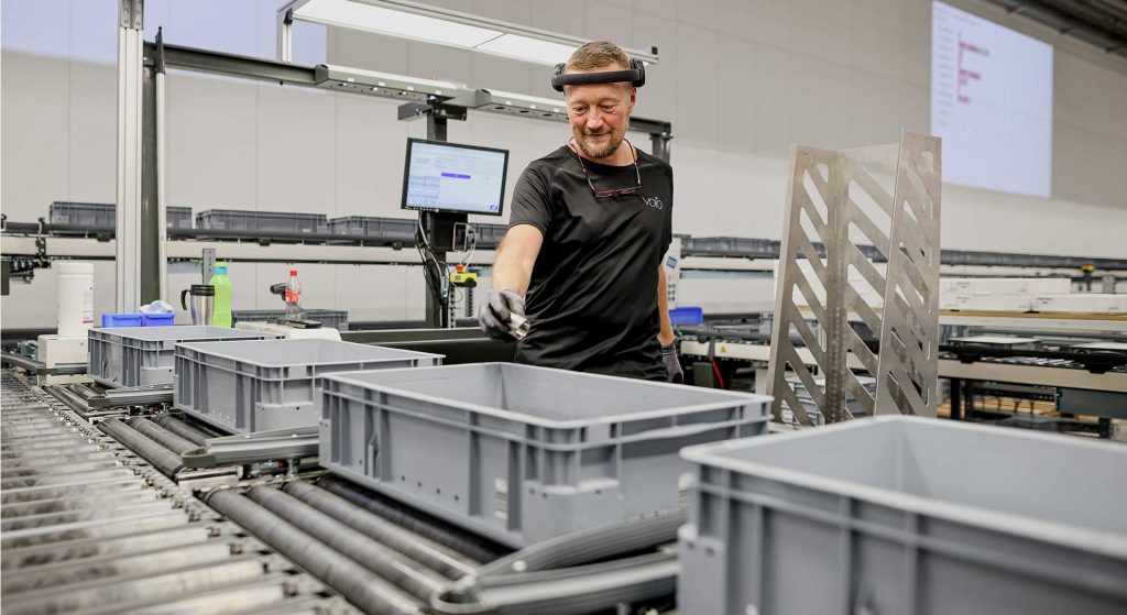 Un employé pose les pièces dans un conteneur en plastique au niveau d’un poste de travail manuel.