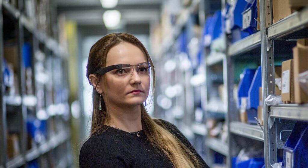 A woman with KiSoft Pick-it-Smart glasses. Pick-it-Smart is a wearable device. The paperless picking technology helps when picking orders. The woman receives important information about the order, such as the storage location, directly on the glass of the KiSoft Pick-it-Smart picking glasses.