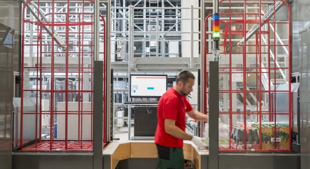 The image shows an ergonomic Pick-it-Easy Case work station. A male employee is assembling an order manually for store delivery.