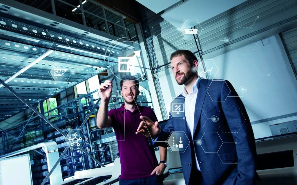 Software & IT-Mitarbeiter bei KNAPP Zwei Mitarbeiter bei KNAPP vor einem grafischen Overlay zum Thema SAP®EWM in der Logistik