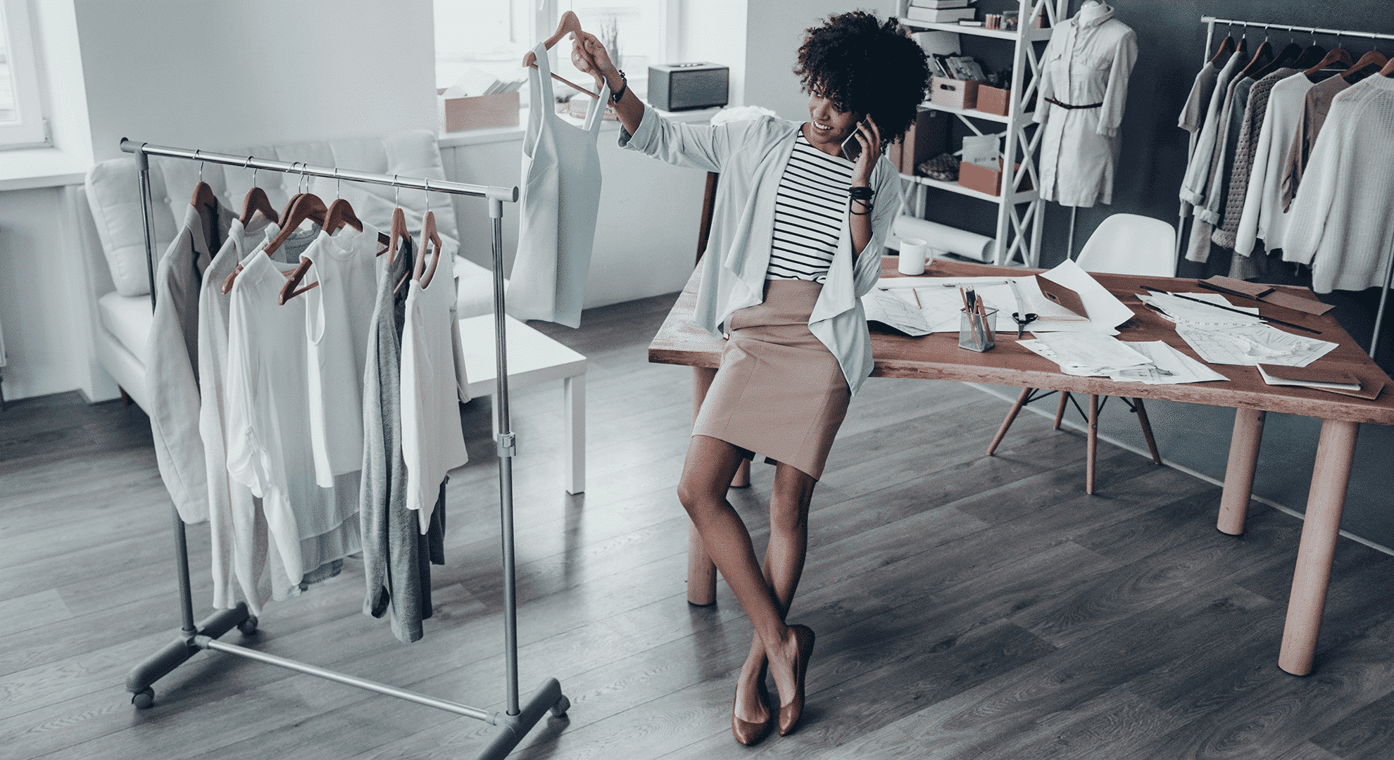 A woman on the telephone, leaning on a desk, selects the perfect outfit from a rack