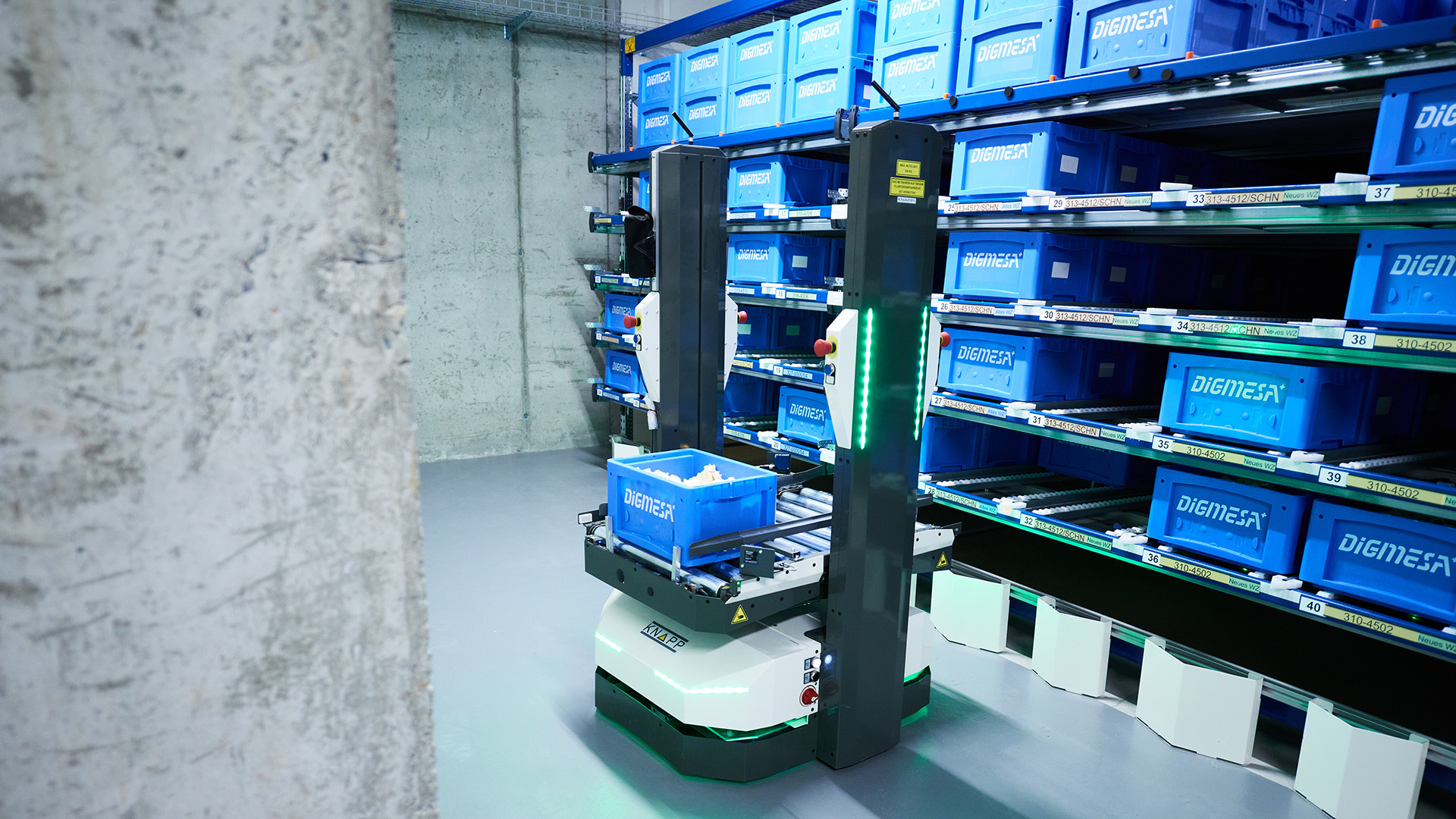 Durch die Integration eines AMR-Systems kann ein Roboterwagen einen blauen DIGIMESA-Behälter durch Lagerregale transportieren, die mit ähnlichen blauen Behältern gefüllt sind.