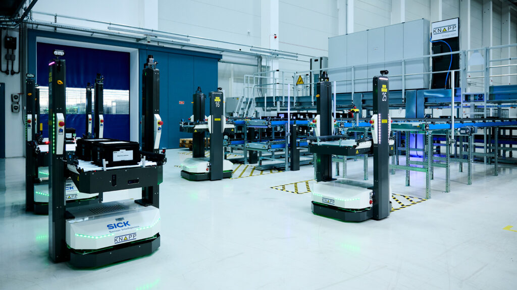 AGV AMR-Systeme transportieren Waren in einem modernen, sauberen Lager mit Förderbändern und Lagerregalen im Hintergrund.