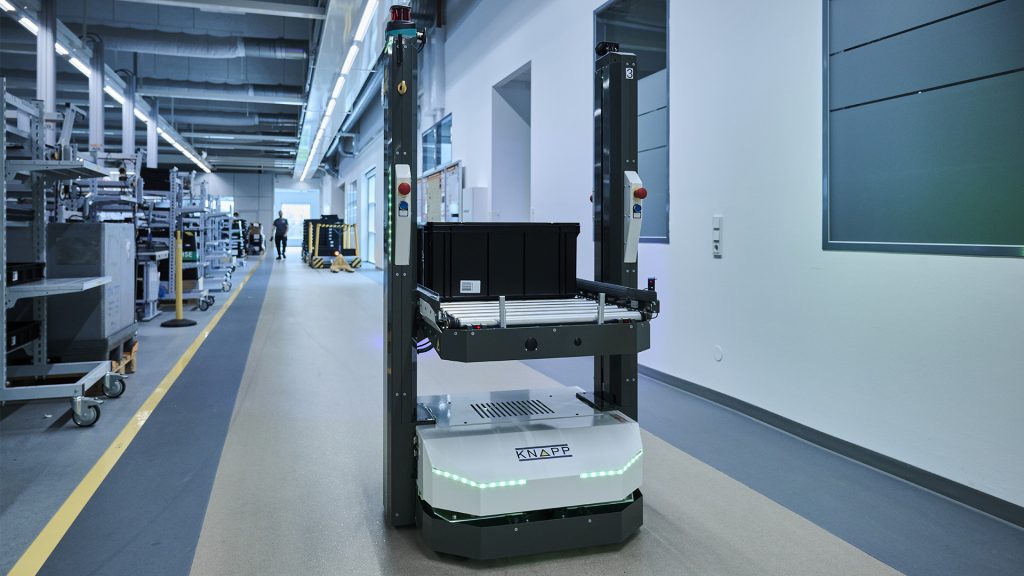 RMA para la automatización en la industria del plástico Un robot móvil autónomo de KNAPP se desplaza una nave de almacén a lo largo de un pasillo.