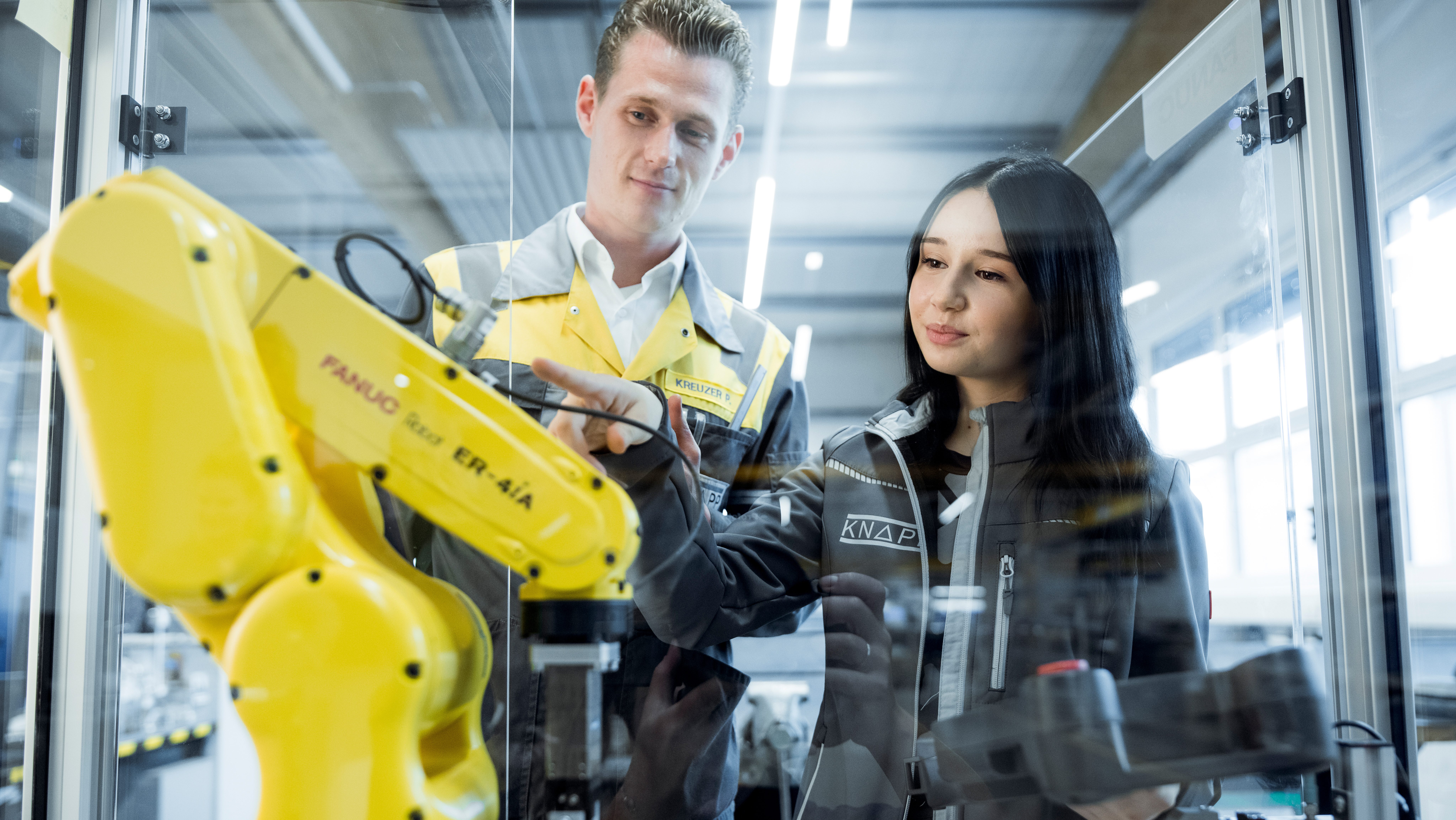 Ein Lehrling betrachtet gemeinsam mit einem Ausbilder einen Industrie-Roboter.