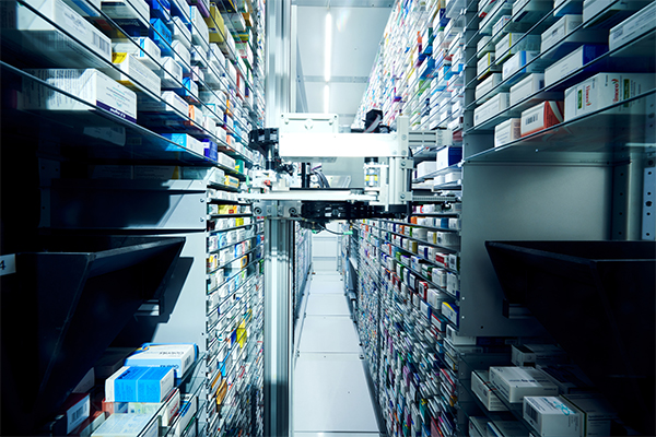 Reihen von ordentlich gestapelten Medikamentenboxen mit einem Roboterarm, der die Ein- und Auslagerung in der innovativen Apotheke Lind automatisiert.