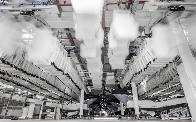 autopocket_inditex_tempe_1 Eine dynamische Ansicht eines automatisierten Sortiersystems, die Reihen weißer Pakete mit hoher Geschwindigkeit in einer modernen Lagerautomatisierungs-Industrieumgebung sortiert.