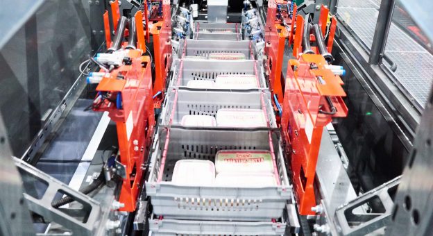 The image shows a fully automatic depalletizing station for the gentle and efficient storing of foods. These robots use a clamping mechanism to separate the containers and place them on the conveyor. These load carriers are automatically transported onwards.