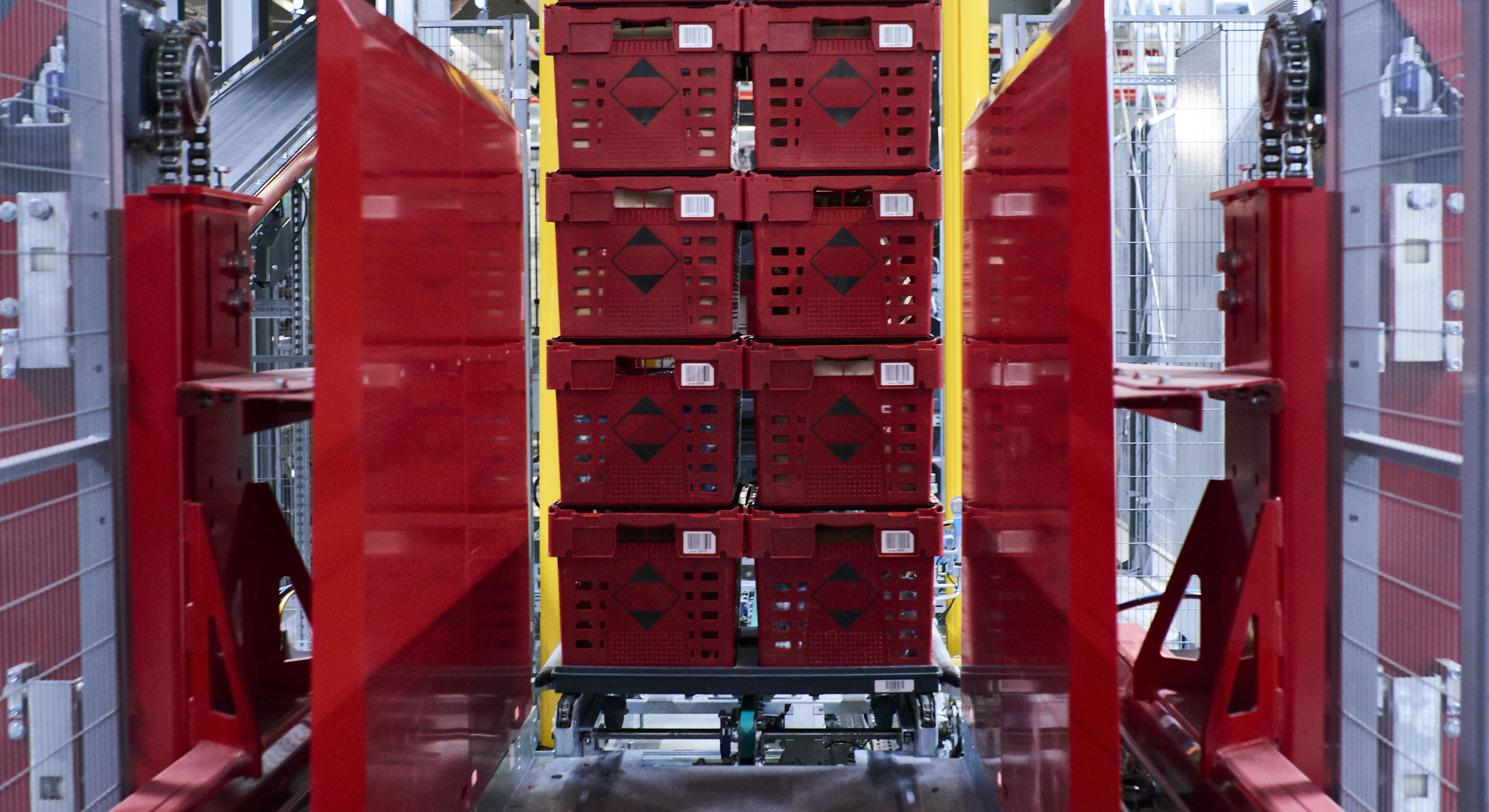 Das Bild zeigt rote Behälter, die mithilfe einer automatisierten Technologie aufeinandergestapelt werden.