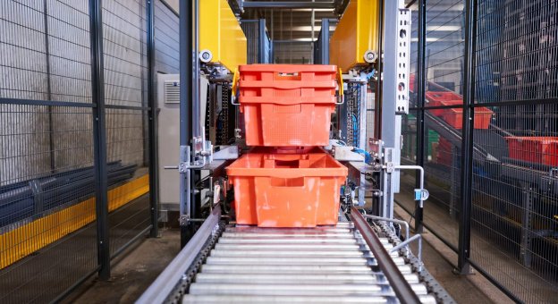 Front view of a fully automatic destacking machine that separates totes for meat and meat products. The tote stacks are transported to the machine on the conveyor system. Clamps grip the totes and separate them. The totes are placed on the conveyor system one by one and move on for further processing.