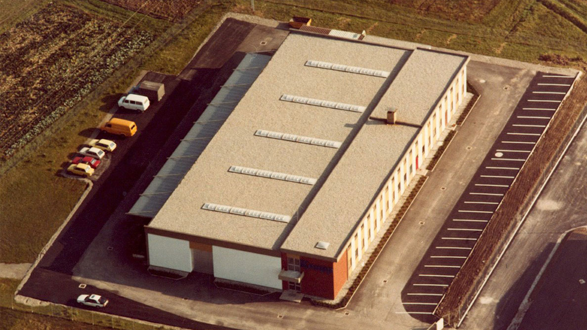 Aerial photo of the rectangular company building, parking lot and green spaces – the new headquarters of KNAPP in 1980.