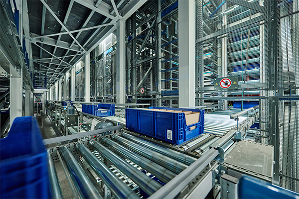 Blaue Kisten bewegen sich auf automatisierten Förderbändern in einem modernen Lager, das Effizienz und Integrationspartnerschaft in der Logistik demonstriert.