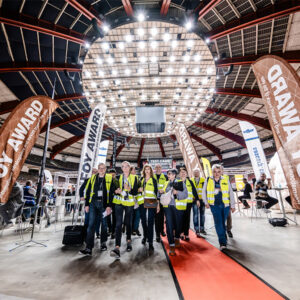 Un grupo con chalecos de seguridad amarillos camina por la alfombra roja de un evento en el que se presentan soluciones de automatización para toda la cadena de valor.