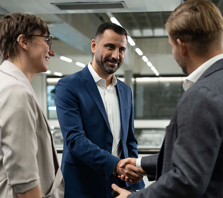 Integration-partner-and-technology-partner-handshake Tres profesionales dándose la mano en una oficina junto a un proveedor de tecnología.