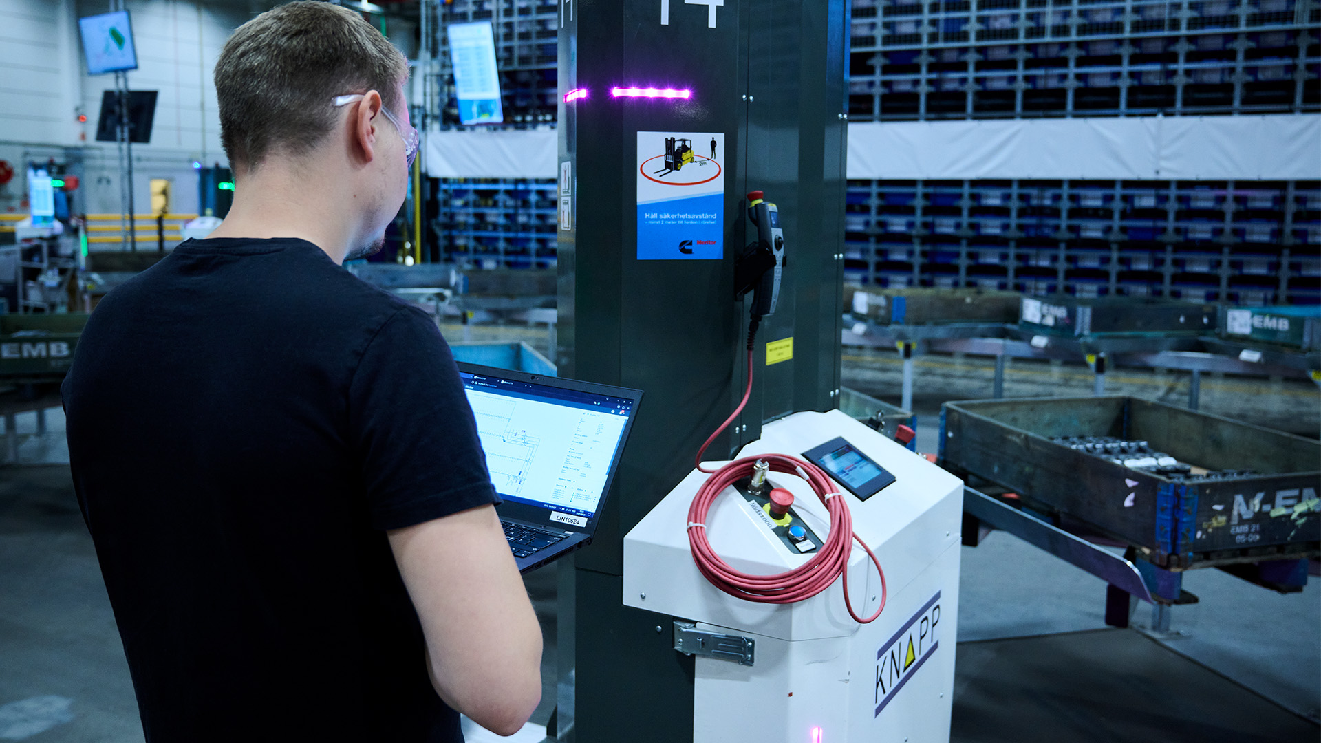 Eine Person nutzt einen Laptop in der Nähe von Industrieanlagen; im Hintergrund sind Container und Metallkonstruktionen zu sehen, was die Integration von AMR in einem Lagerhaus verdeutlicht.