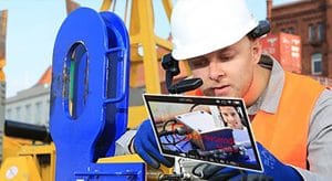 A man with a safety helmet is looking at a tablett. He is talking to a person who is remotely connected with him via a video stream.