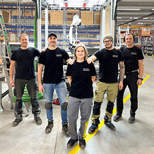 Five people in black KNAPP T-shirts in a warehouse are smiling into the camera.