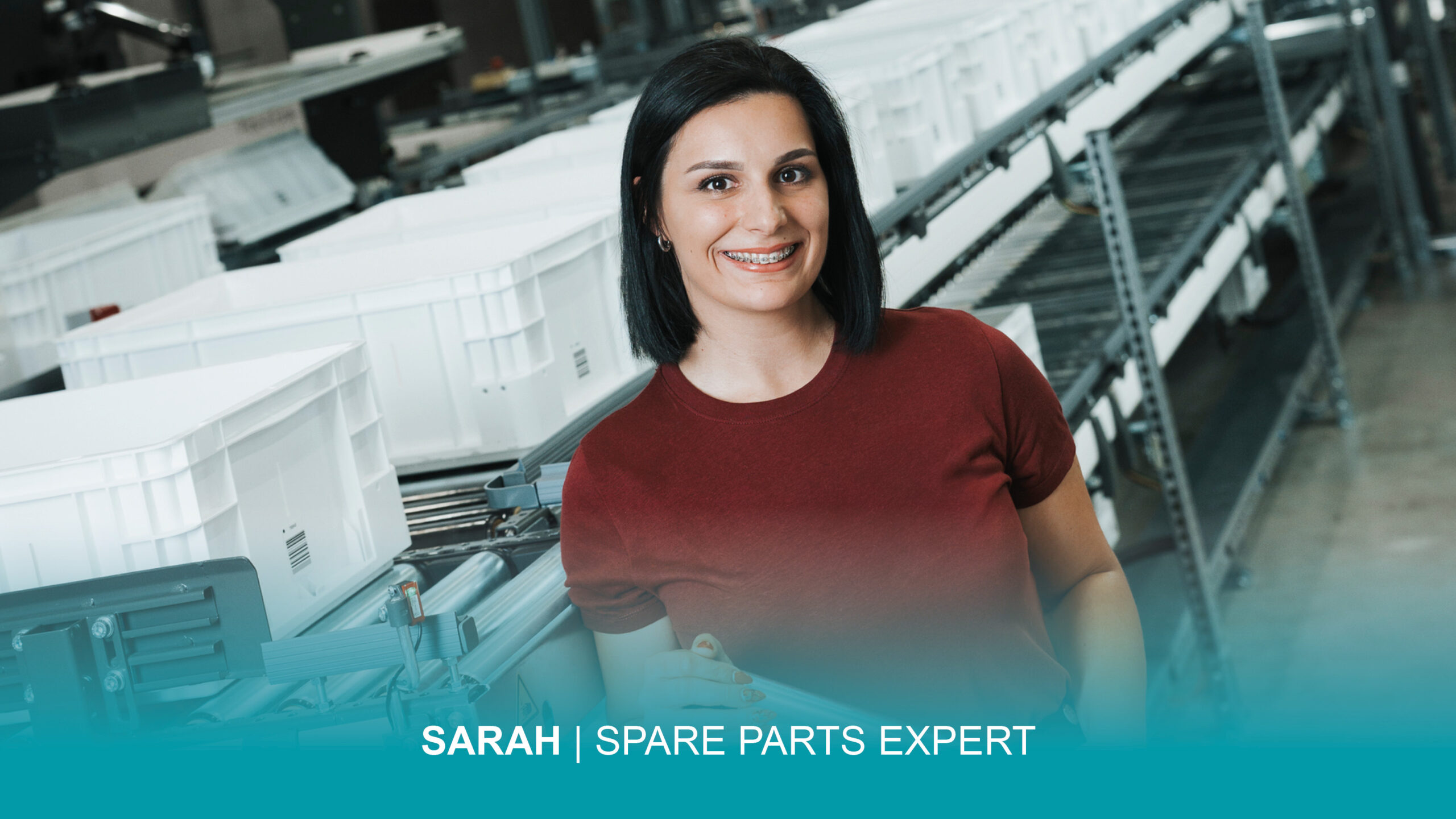 Eine Frau im roten Hemd lächelt, während sie vor einer Fördertechnik steht. Im Bild ist folgender Text integriert: "Sarah | Spare Parts Expert.