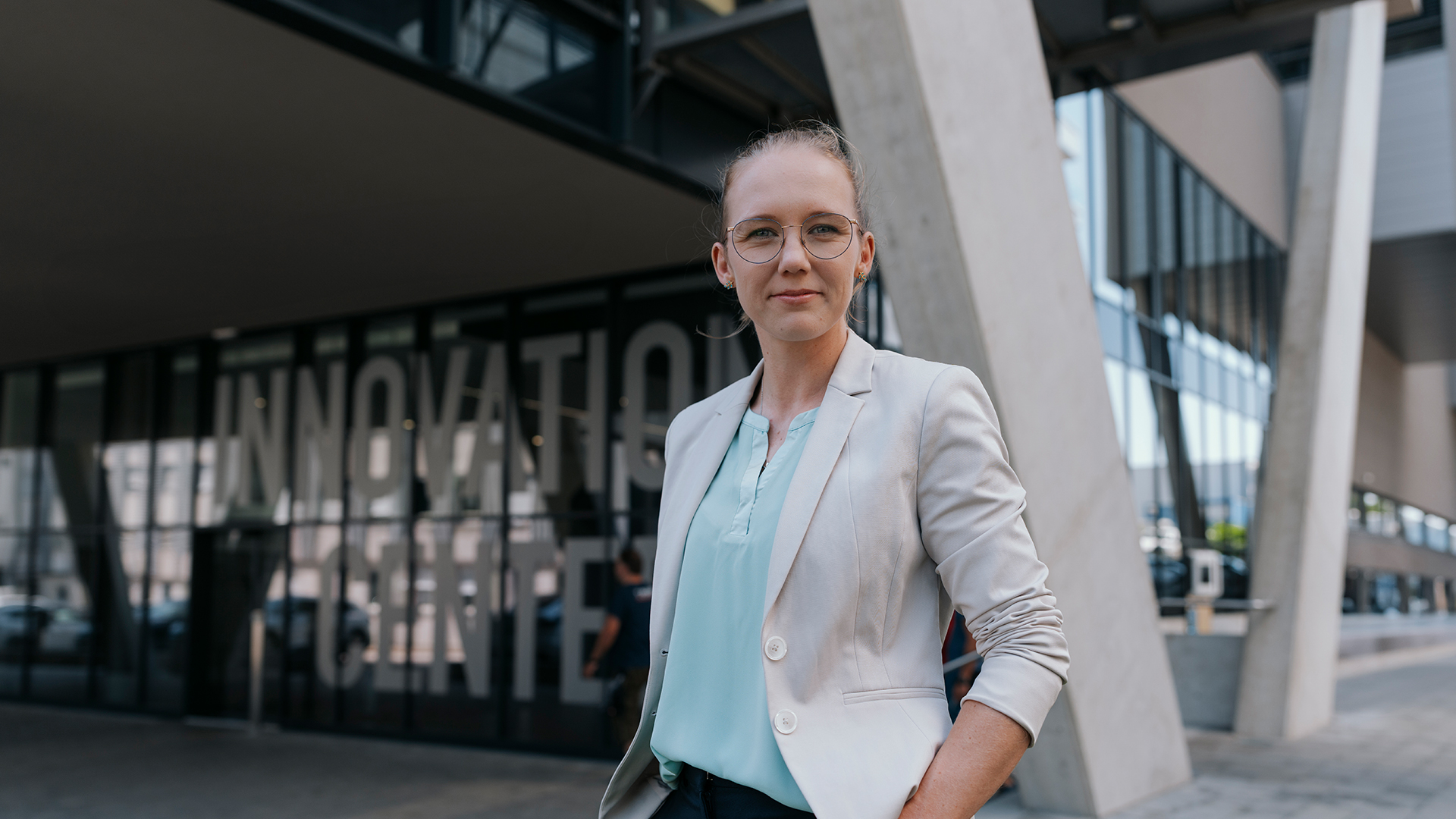 Eine selbstbewusste Person in einem hellen Blazer steht vor einem modernen Gebäude.