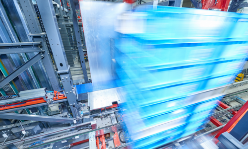 Shipping preparation EDEKA NORDfrische A high-angle view of a motion-blurred stack of blue plastic crates being moved by an industrial automated conveyor system in a warehouse.