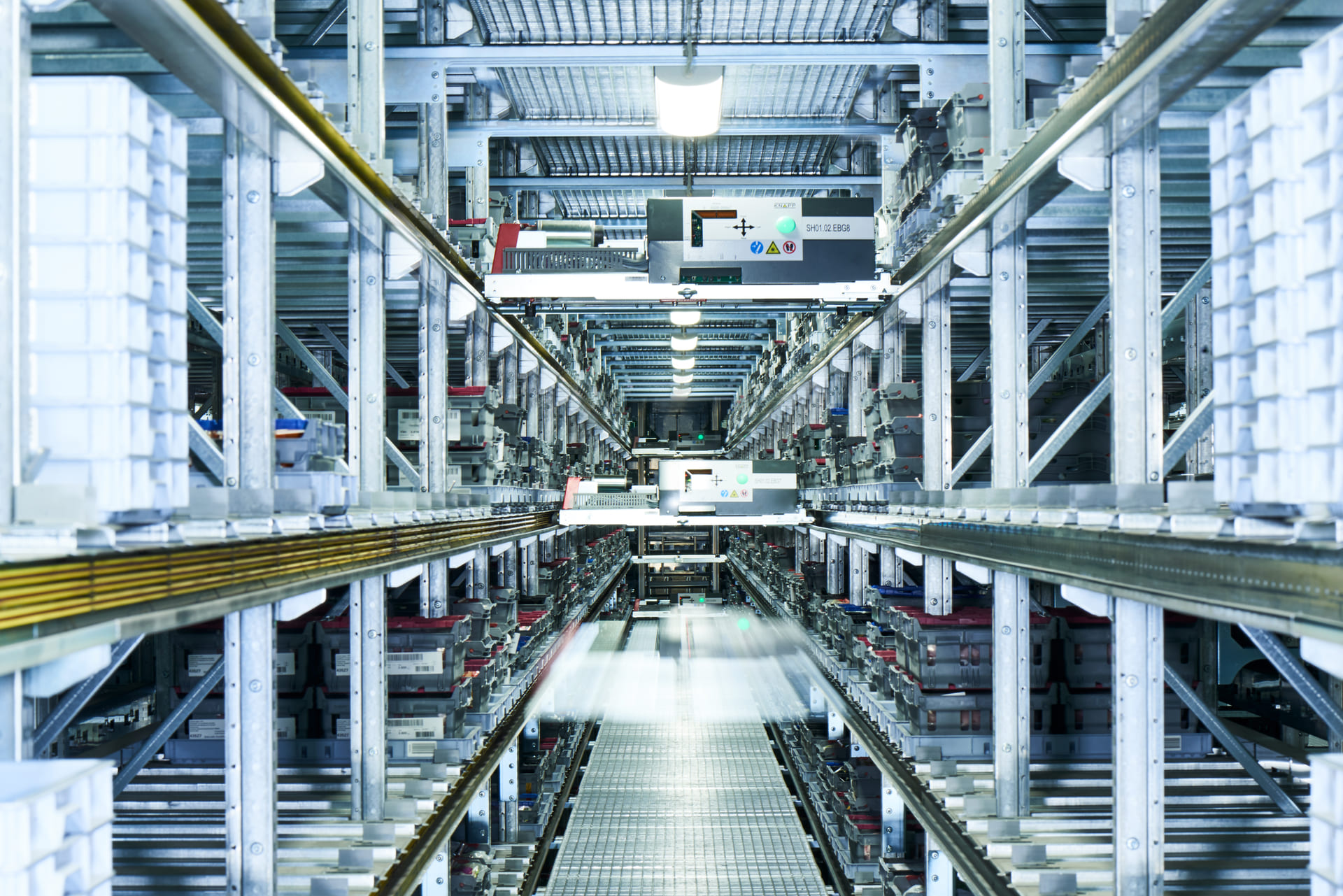 Ein modernes automatisiertes Lager mit Reihen von Regalen mit weißen Kartons, Förderbändern und Robotern, die die Artikel für die Filialbelieferung effizient auf Metallschienen unter heller Industriebeleuchtung bewegen.