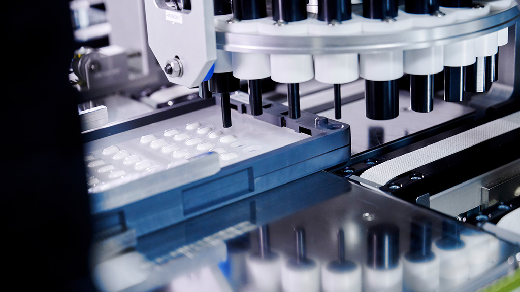 Vista en detalle de una máquina farmacéutica que está extrayendo automáticamente comprimidos de un blíster.