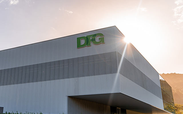 KNAPP-DFG San Sebastian 18-RGB_Medium_640x400 Bâtiment moderne blanc avec le logo "DFG", soleil brillant derrière la structure et ciel dégagé en arrière-plan.