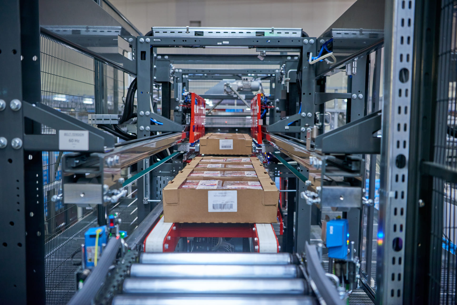 Dans un entrepôt, un système de convoyage permet de déplacer des cartons. Des machines automatisées et des rails métalliques guident les colis tout au long du processus.